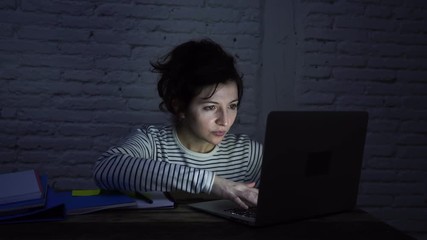  Female brunette sitting at the computer laptop at night. Scroll on touchpad and typing on keyboard happy finishing work report or essay. In working at home and final exams concept.