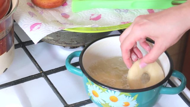 A woman is cooking American donuts. Bake them in sunflower oil. Nearby are cooked donuts