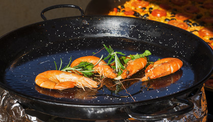 Huge fry pan with few shrimps embellished with parsley and rosemary herbs at street food market in Prague, Europe. Sunny day.