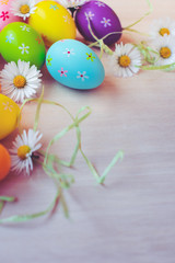 Obraz na płótnie Canvas Close up and top view of colorful painted easter eggs decoration with fresh white blooming daisies on wooden background. Happy Easter background