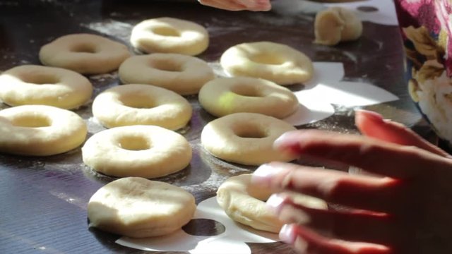 A woman makes blanks for American donuts. Made of dough, lie on the surface of the table. Nearby are tools for cooking..