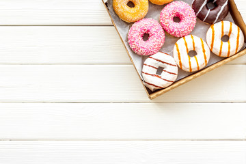 Glazed decorated donuts in box for sweet break on white wooden background flat lay copy space
