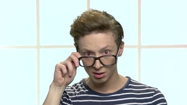 Teenage boy in eyeglasses looking surprised. Surprised nerdy boy close up. Checkered window background.