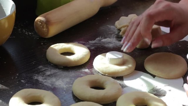 A woman makes blanks for American donuts. Made of dough, lie on the surface of the table. Nearby are tools for cooking