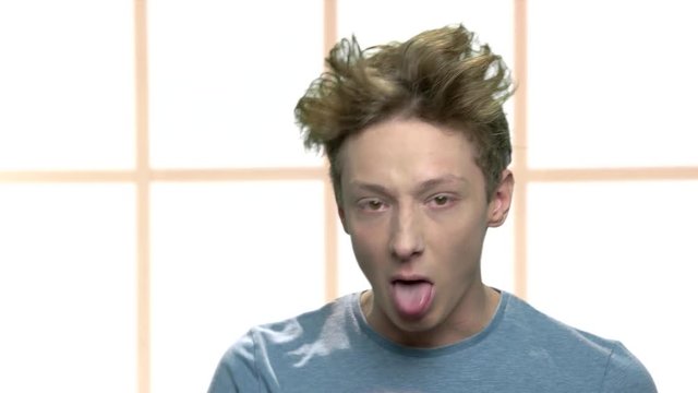 Rude teenage boy teasing somebody. Teen boy with crazy hair sticking out tongue and showing grimace close up.