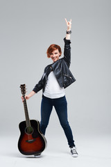 Young woman musician in a black leather jacket with an acoustic guitar in hand on a gray...