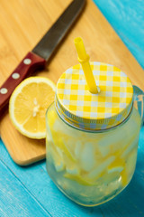 Water with lemon. Lemonade with lemon slices, jar with straw on blue wooden background.