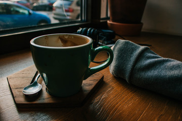 Closeup of a girl at cafe holding a cup of cappuccino coffee. Millenial styled photo in cozy atmosphere