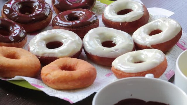 American donuts, glazed with melted chocolate, lie on a platter. Next to the containers melted chocolate.
