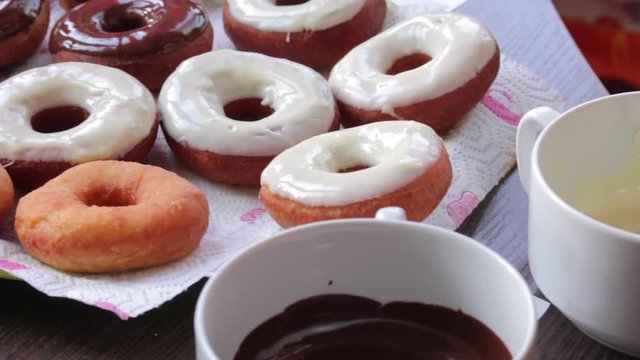 American donuts, glazed with melted chocolate, lie on a platter. Next to the containers melted chocolate