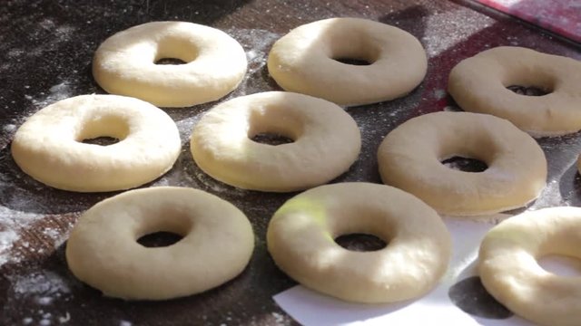 Blanks for American donuts. Made of dough, lie on the surface of the table. A woman sprinkles them with flour. Nearby are tools for cooking.