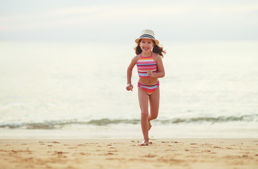 happy child girl  with swimsuit and hat  on  beach at sunset.