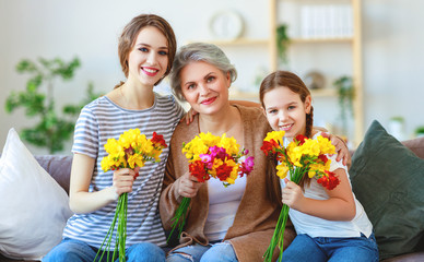 Fototapeta na wymiar three generations of happy family grandmother, mother and daughter with flowers at home