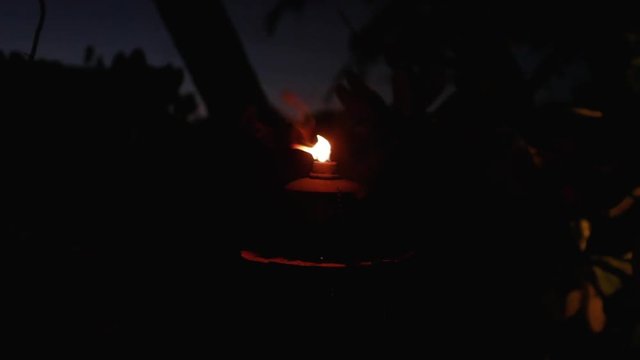 An outdoor lantern flickers and jumps in the darkness; luxury tropical resort.
