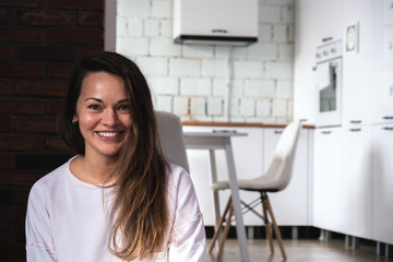 Young smiling woman sitting on the floor in the living room opposite the kitchen