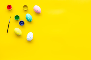 Colorful Easter eggs and paint for celebration on yellow background top view mock up