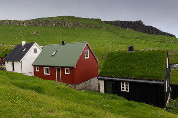 Small Faroe Islands dwellings including a traditional turf roofed house in rural landscape with mountains in the background