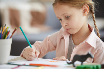 Portrait of cute girl drawing pictures sitting at table home alone, copy space