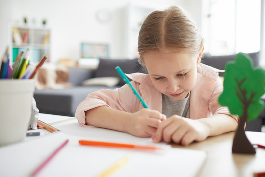Portrait of cute girl doing homework at home learning to write with pencil, copy space