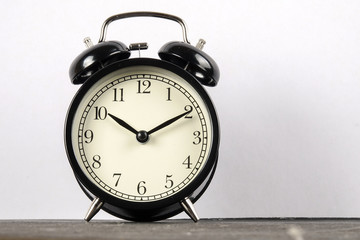 Black alarm clock on the wooden surface against the white background.