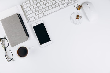 Flat lay, top view modern office table desk. Workspace with glasses, smartphone, keyboard, office supplies, pencil, green leaf, and coffee cup on white background