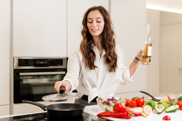 Brunette woman preparing fresh fish steak on the kitchen with vegetables and glass of white wine. Housewife concept