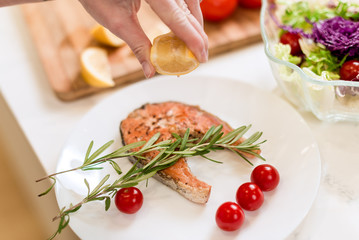 Brunette woman preparing fresh fish steak on the kitchen with vegetables. Housewife concept