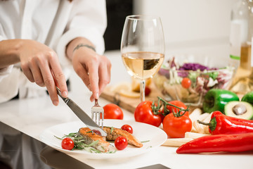 Woman preparing fresh fish steak on the kitchen with vegetables and glass of white wine