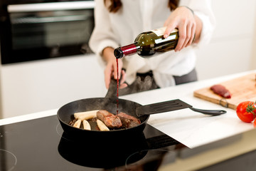 Brunette woman cooking and eating red meat steak with glass of red wine. Housewife concept