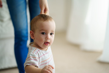 baby boy doing first steps with mother's support. baby boy doing first steps. mom and toddler son playing in living room. motherhood, family, love, parenthood, early development