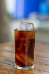 Cola soda with ice in glass on wooden table