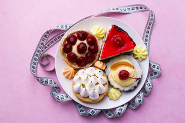 proper nutrition, healthy lifestyle, diet, carbs reduce, sugar, sweets. pink background with delicious cakes and measure tape. fitness, nutritionist, dietitian blog design concept