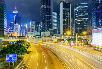 Fototapeta na wymiar Street traffic in Hong Kong at night. Office skyscraper buildings and busy traffic on highway road with blurred cars light trails. Hong Kong, China