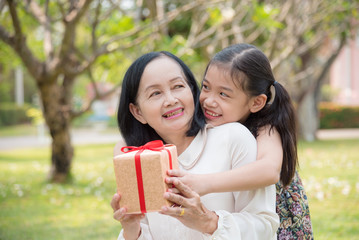 Asian granddaughter giving birthday gift for granddaughter in the garden.Happy Asian family conception.