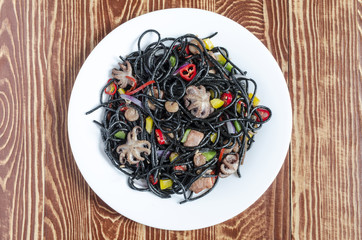 spicy black spaghetti with seafood and vegetables on a white plate brown wooden background top side view close-up