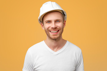 Portrait of enthusiastic man, smiles broadly, laugh joyfully at funny rumor, wears work clothes with a helmet. Isolated on white background in studio