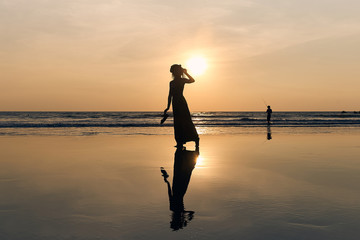 Fototapeta premium Contrast silhouette of a young slender woman against the background of a Sunny sunset, the sea and the sandy beach. 