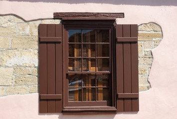 A brown wood window set against a pink wall with light stones from the wall shoing