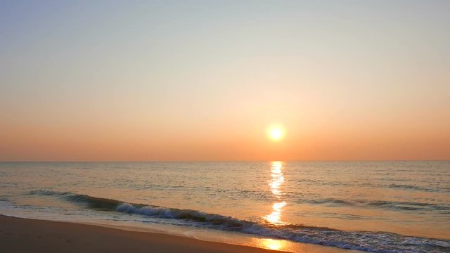 Static wide shot of a beautiful sunrise with waves gently rolling at a lonely beach.