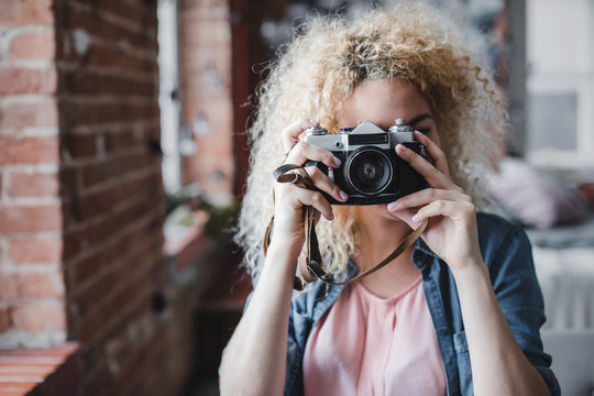 Curly blonde woman holding her retro photo camera at home.