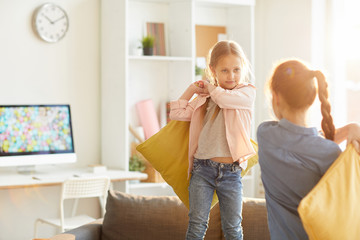 Portrait of two sisters playing pillow fight standing on sofa, copy space