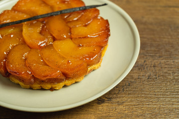 Freshly baked homemade Apple Tarte Tatin with a vanilla pod on a gray plate on a wood table top.