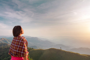 Rear view of a young woman standing on a mountain top peacefully gazing at low-lying morning clouds with copy space.