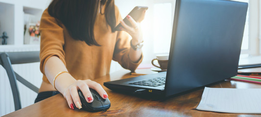 Closeup of hand asian businesswoman using mouse to working with laptop and holding smartphone to connect online