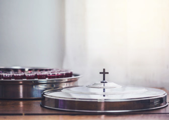 selective focus of the cross on communion tray cover with a wine glasses  in communion tray on wooden table with window light, christian background with copy space