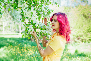 Beautiful and young woman with bright red hair and ref lips standing next to a blooming apple tree...