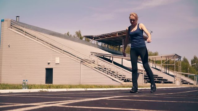 Young cute girl, sporty physique, at stadium. She does the warm-up of the muscles, before training.