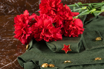 on the marble slab of the monument, there is a bouquet of carnations on a military uniform and a cap with a red star