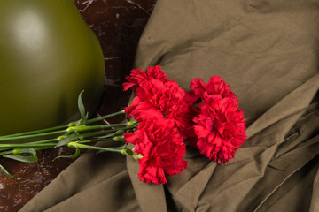 on a marble slab, a bouquet of red carnations, a military helmet and a cloak tent