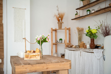Summer kitchen interior in rustic style. Bright kitchen with a wooden table. Spring flowers and bread in a basket on the table in the kitchen